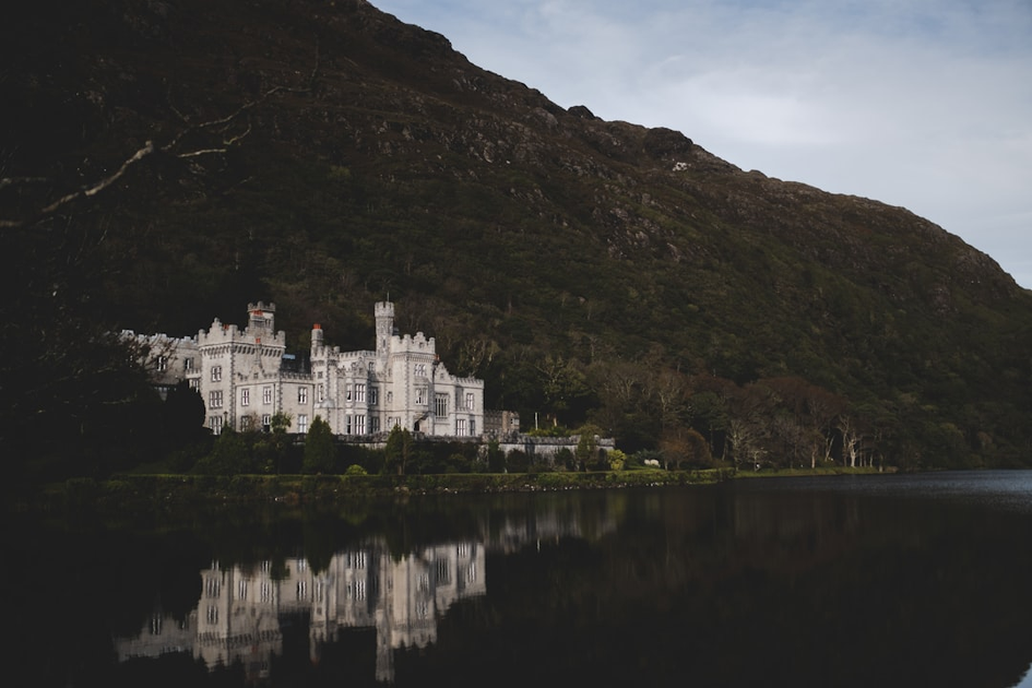 Historic Irish castle with stone towers reflected in lake with jaunting car and tourists