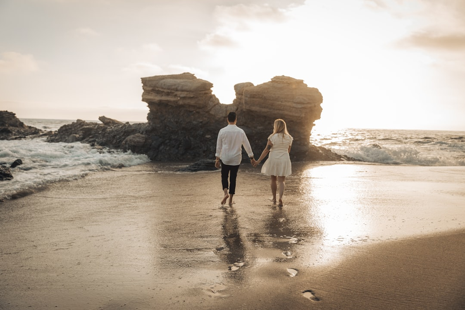 Romantic couple walking hand-in-hand on pristine white sand beach at sunset, symbolizing the start of their luxury honeymoon journey together