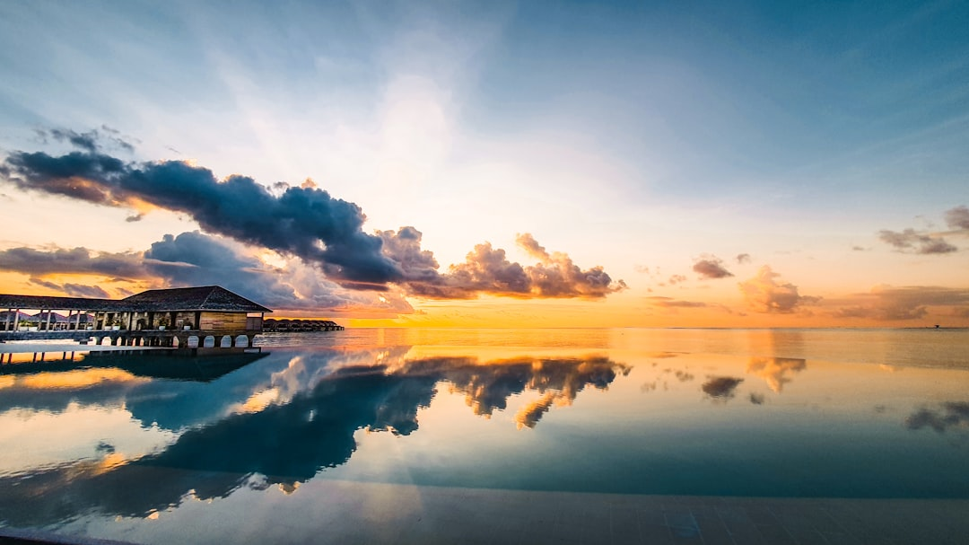 Luxury overwater bungalow villa in the Maldives at sunset with couple watching romantic golden hour sky over turquoise lagoon